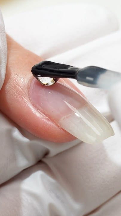 A bead of hard gel builder being applied to a natural nail.