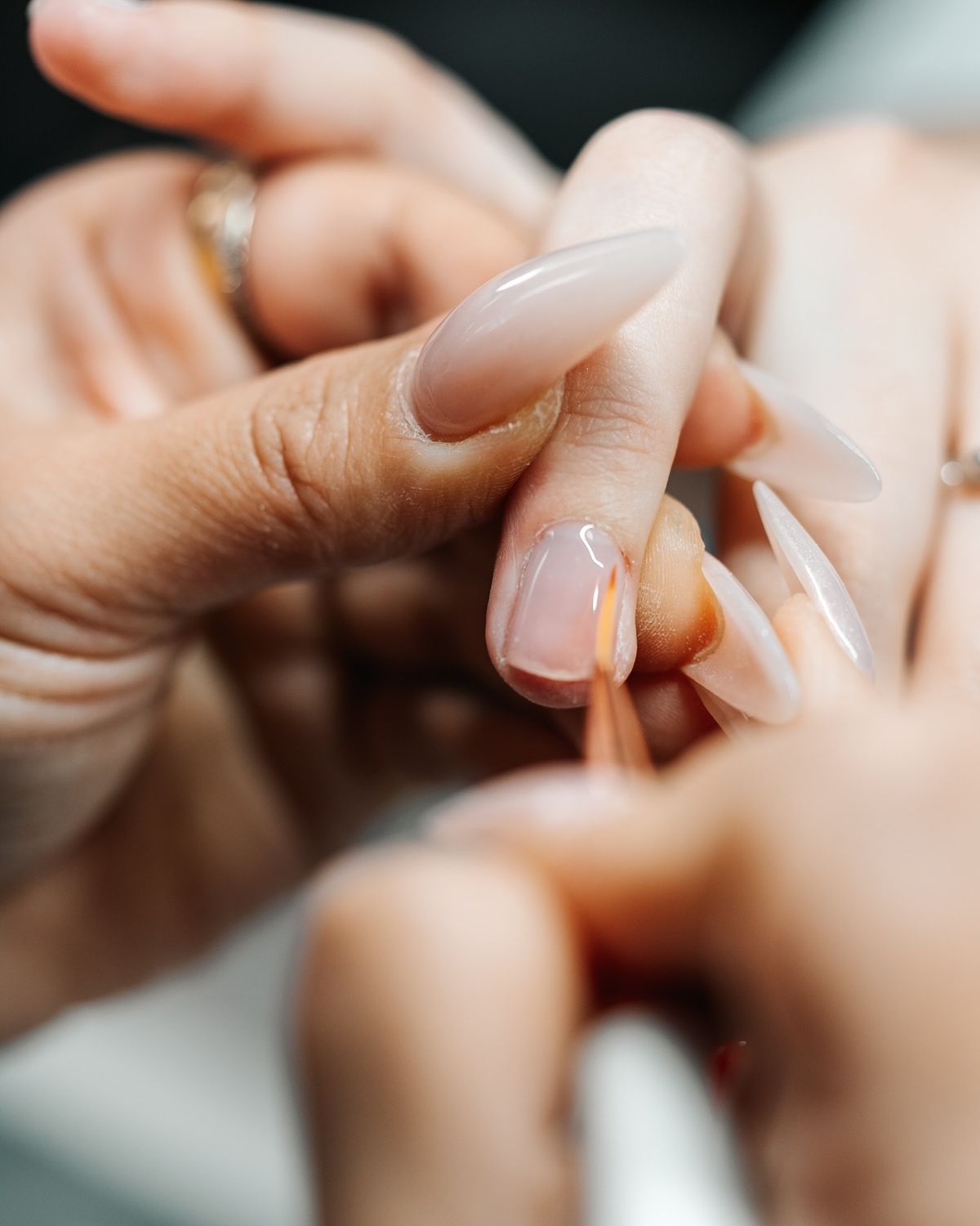 A nail artist brush-applying hard gel to a natural nail, with milky almond nails in progress.