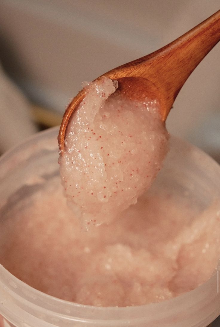 A wooden spoon of rose sugar scrub over an open jar.